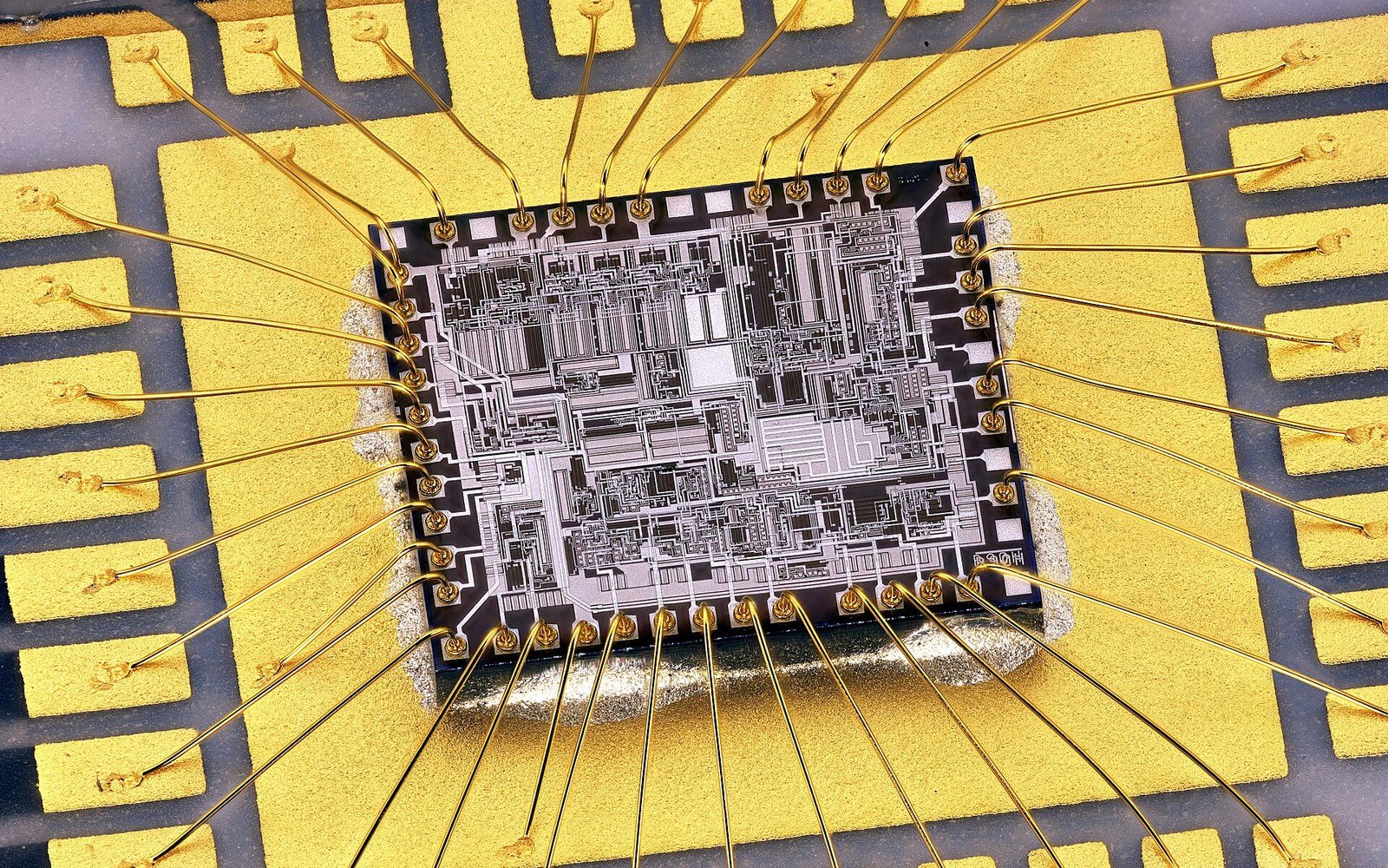 Close-up of an integrated circuit die connected by gold bond wires to a chip package