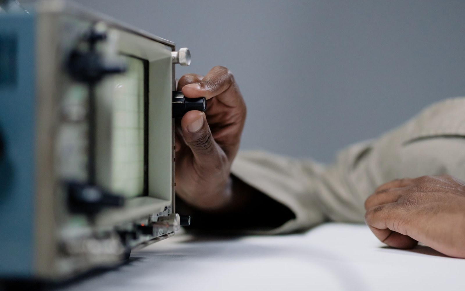 A hand adjusts a knob on an old oscilloscope resting on a workbench